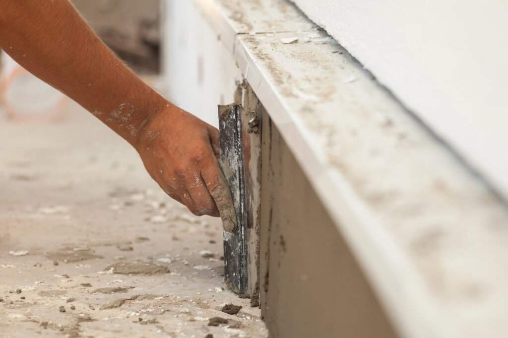 A man's hand plastering foundation of a house