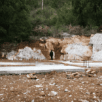 Concrete slab on grade foundation under construction with exposed soil and footing layout before residential home building begins.