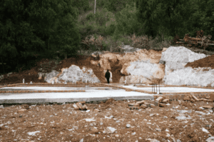 Concrete slab on grade foundation under construction with exposed soil and footing layout before residential home building begins.