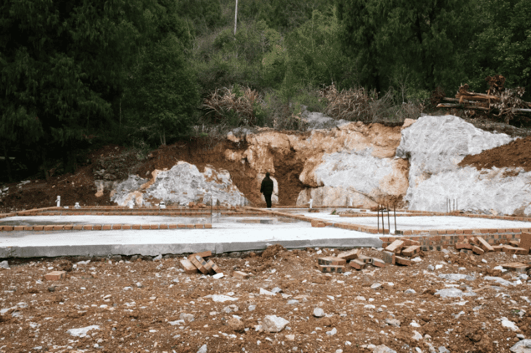 Concrete slab on grade foundation under construction with exposed soil and footing layout before residential home building begins.