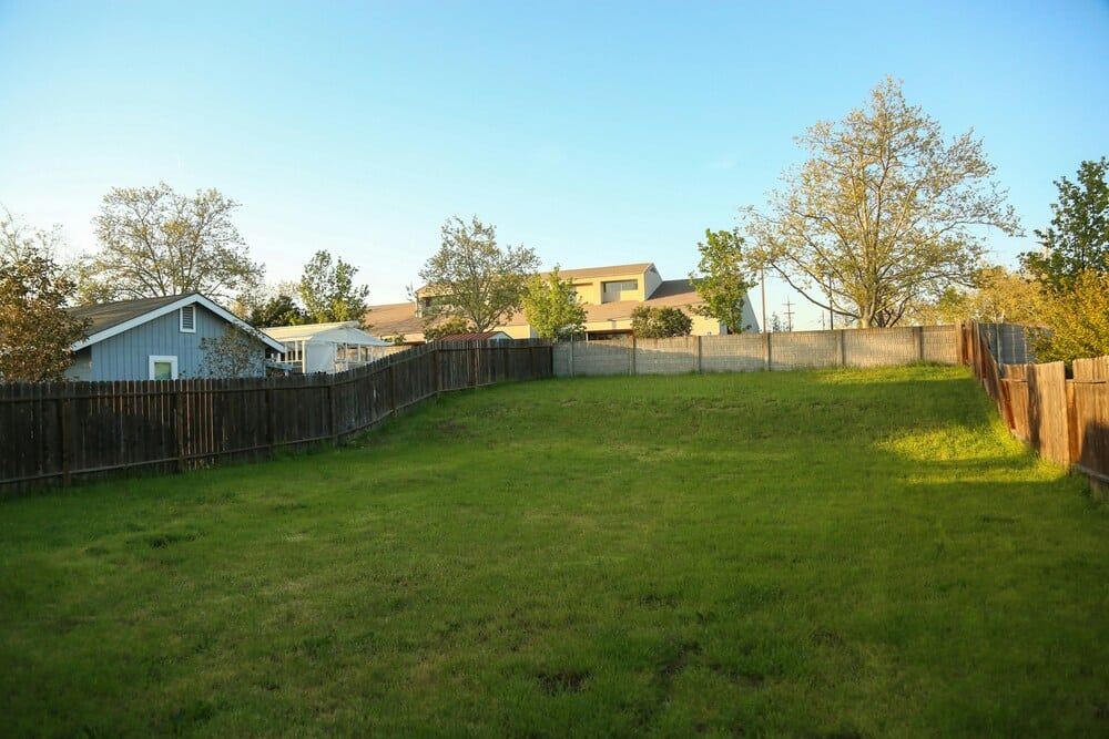 A wide shot of a spacious, clear green backyard lawn enclosed by a wooden fence under a bright blue sky, illustrating an ideal unobstructed path for heavy machinery access.