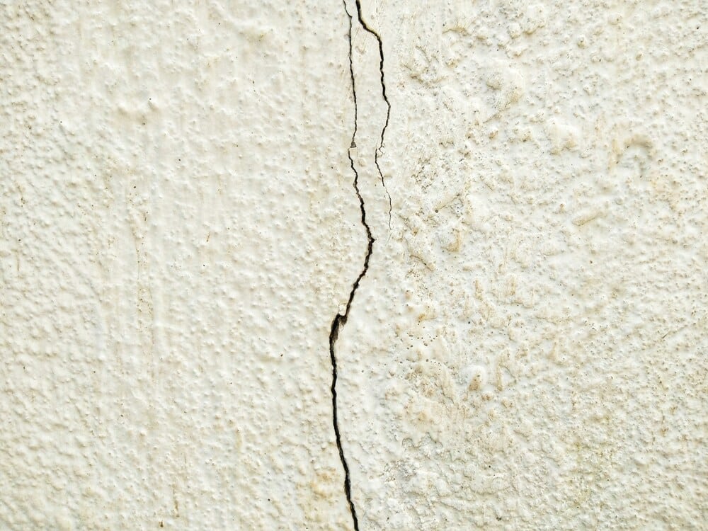 A close-up of a distinct vertical crack running down a textured concrete foundation wall.