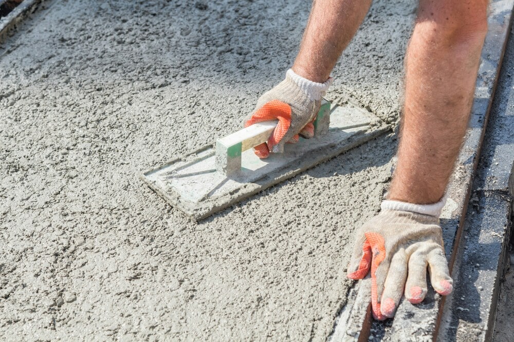 A close-up of a worker's arms using a rectangular trowel or hand float tool to meticulously level out a fresh wet concrete patch, demonstrating the professional stabilization and concrete repair techniques used to secure a home's equity.
