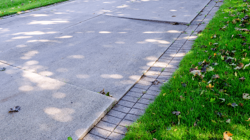 Residential concrete driveway with joints and edging near a lawn.