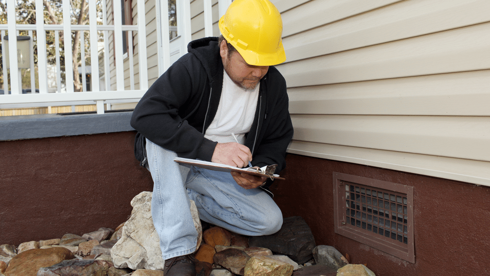 Contractor inspecting a home foundation area and crawl space vent during a spring check.