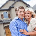 Smiling couple standing in front of their suburban home, confident their foundation and exterior are ready for the fall season.